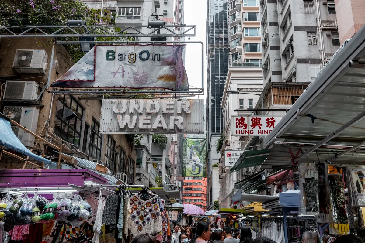Vibrant street market scene in Hong Kong with shops and diverse signage, embodying urban life.