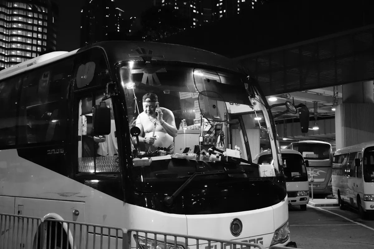 Black and white photo of a bus driver at night in Hong Kong terminal.