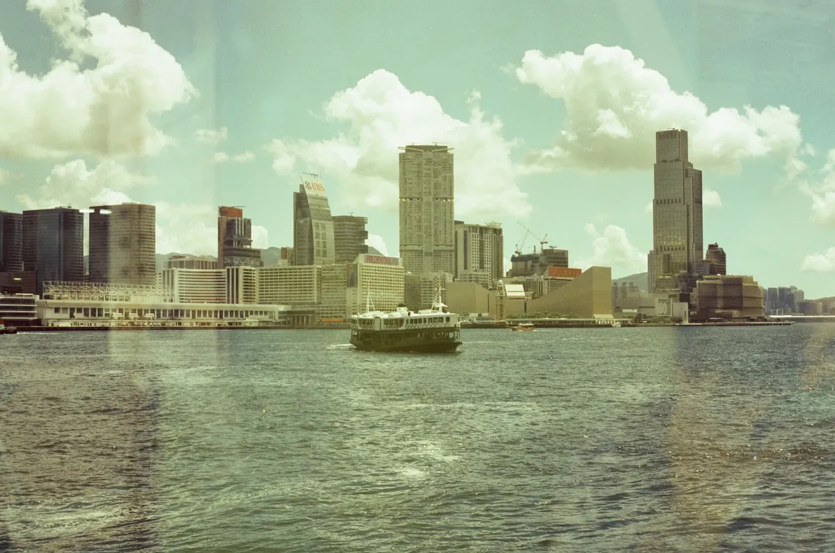 Scenic day view of Hong Kong harbour featuring skyline and ferry.