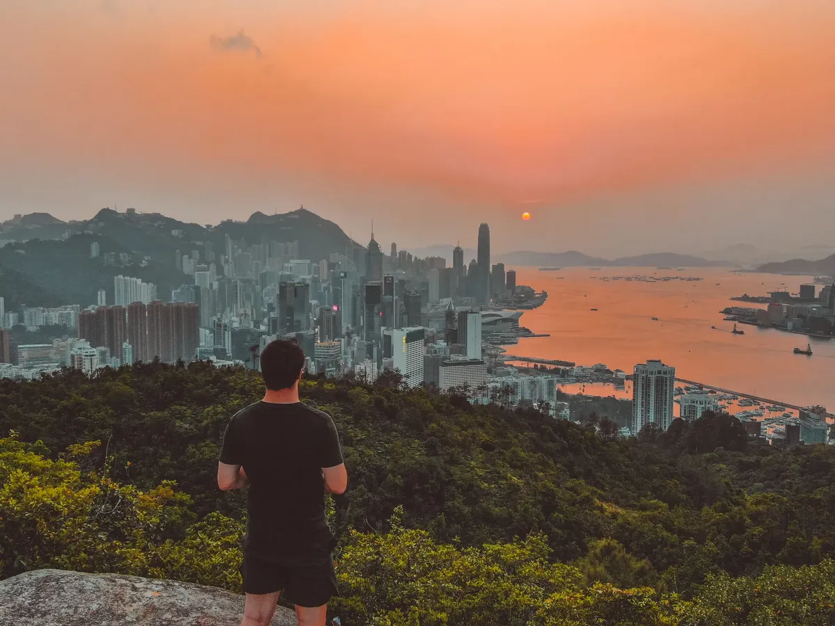 ブラーム hill 上に立つ若い男性の後ろ姿。夕陽の空の下、海と香港島の美しい風景を眺めている。