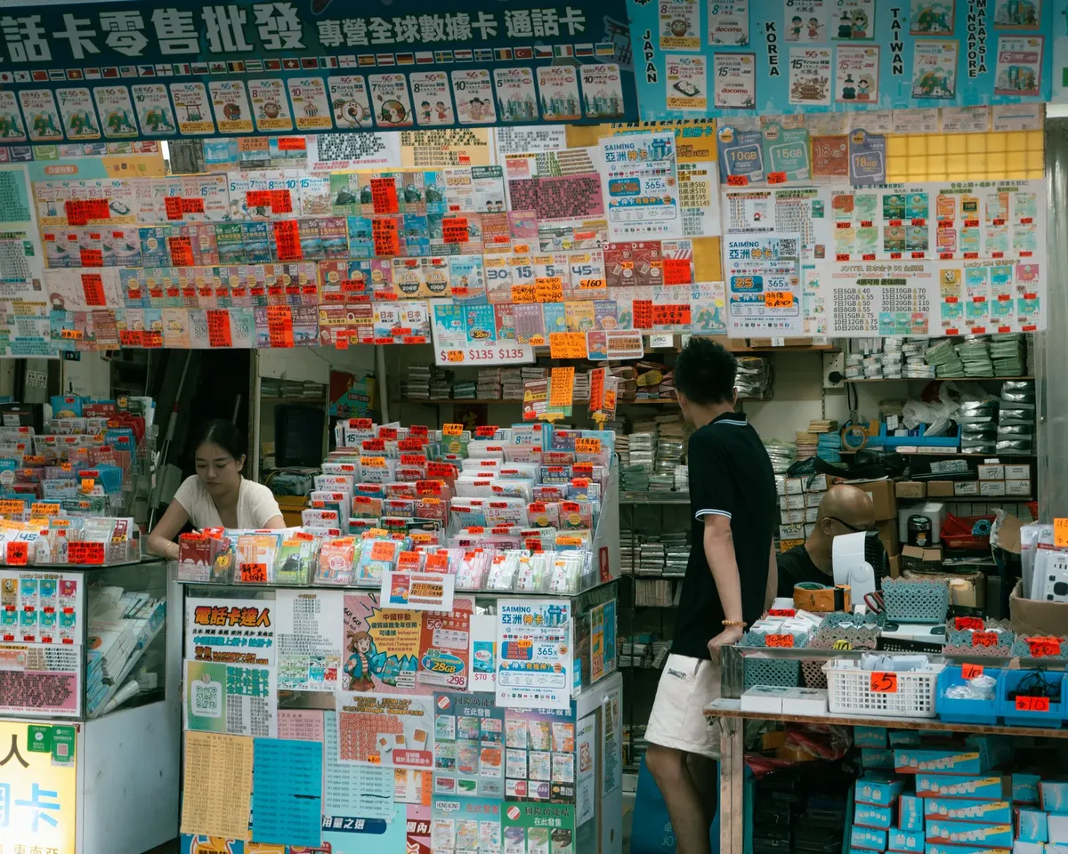 Colorful market stall selling phone cards in Kowloon, Hong Kong, bustling with activity.