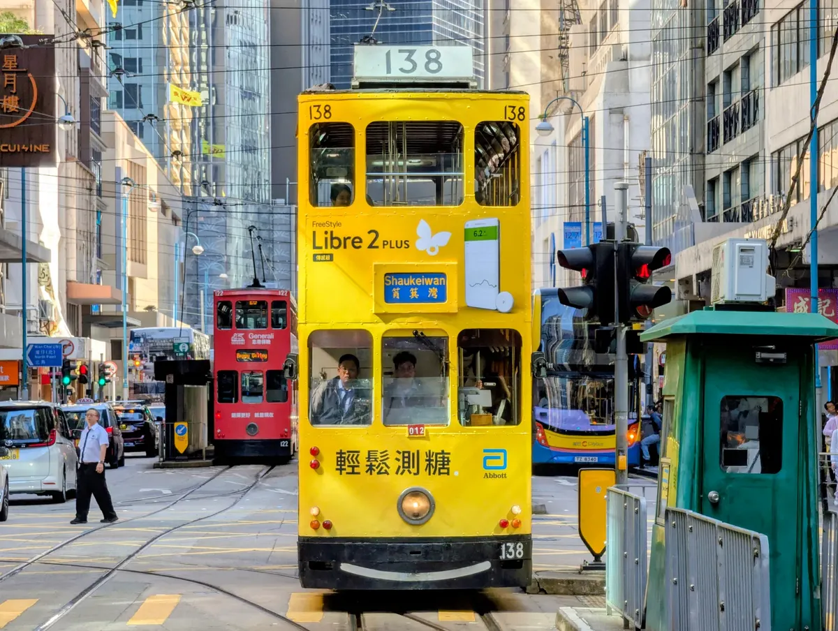 Vibrant yellow tram passing through Hong Kong's bustling streets, capturing urban life and architecture.