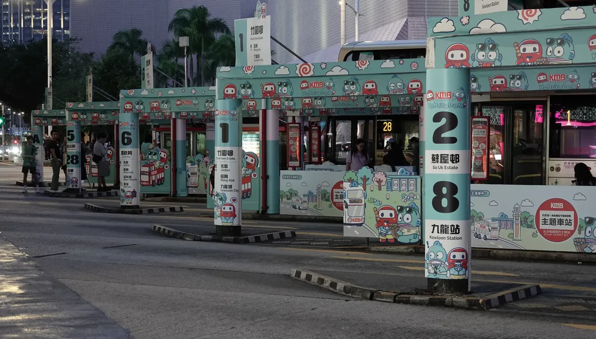 Colorful bus stop scene in Kowloon, Hong Kong, featuring cartoon themed signage and waiting passengers.
