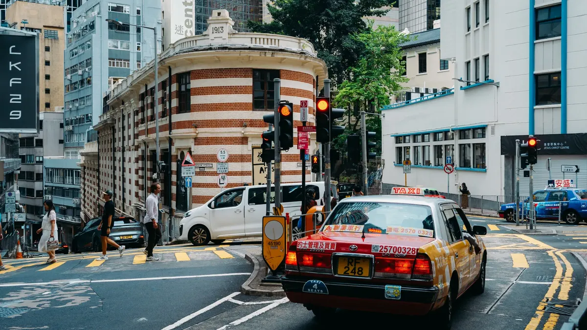 A busy urban street scene in Central Hong Kong featuring pedestrians and a taxi.
